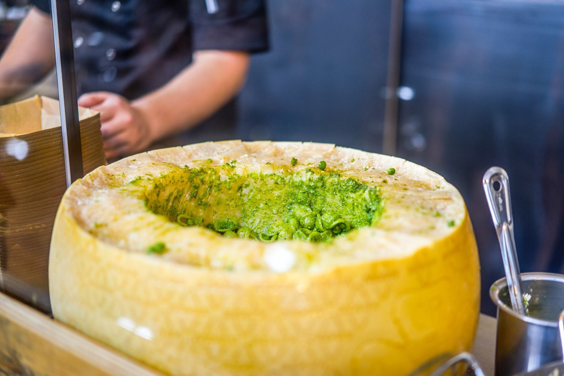 Archive photo of Pasta Face finishing green pasta in a large Parmesan cheese wheel at an event