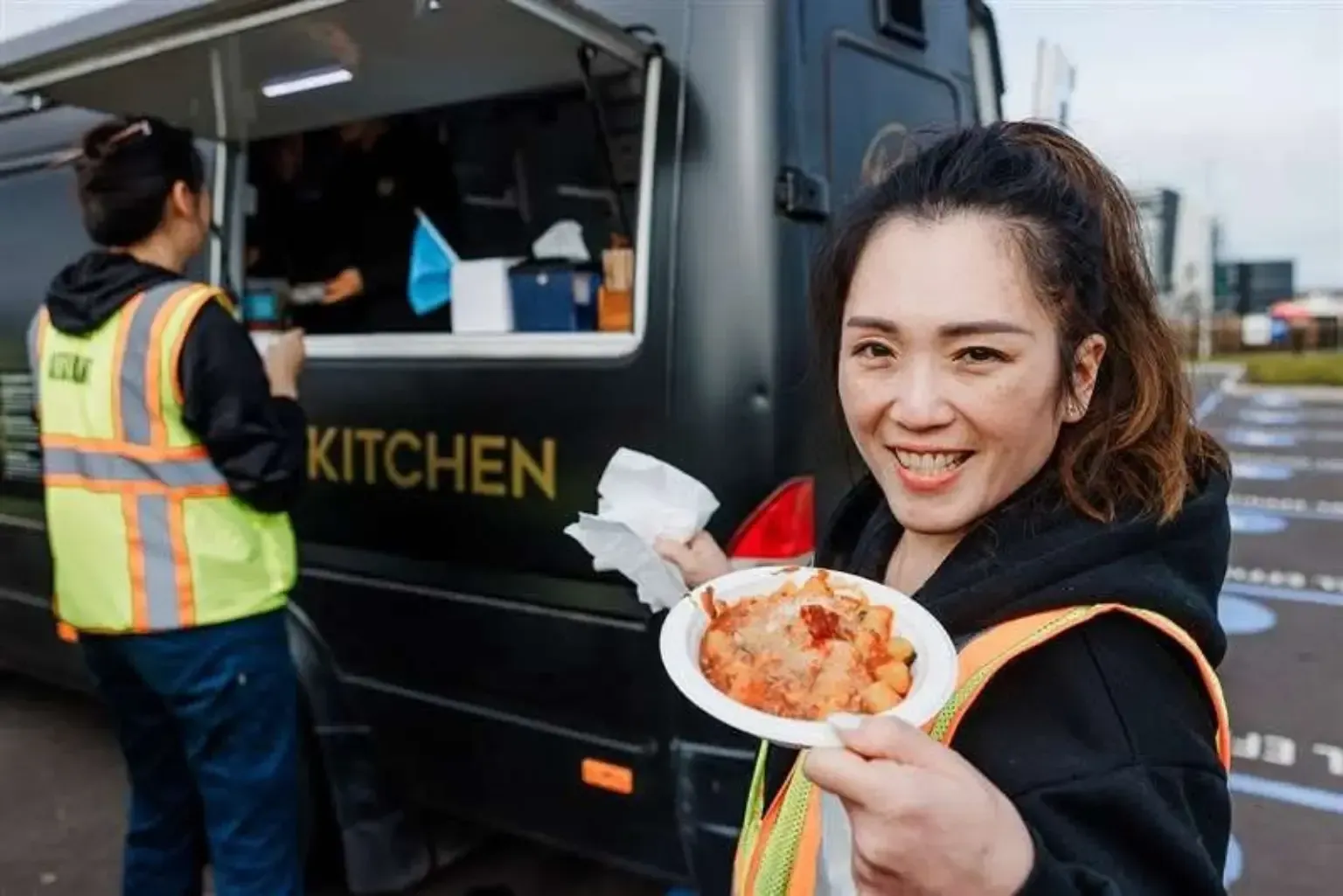 Industrial employee holding a freshly prepared pasta meal beside the Pasta Face mobile kitchen