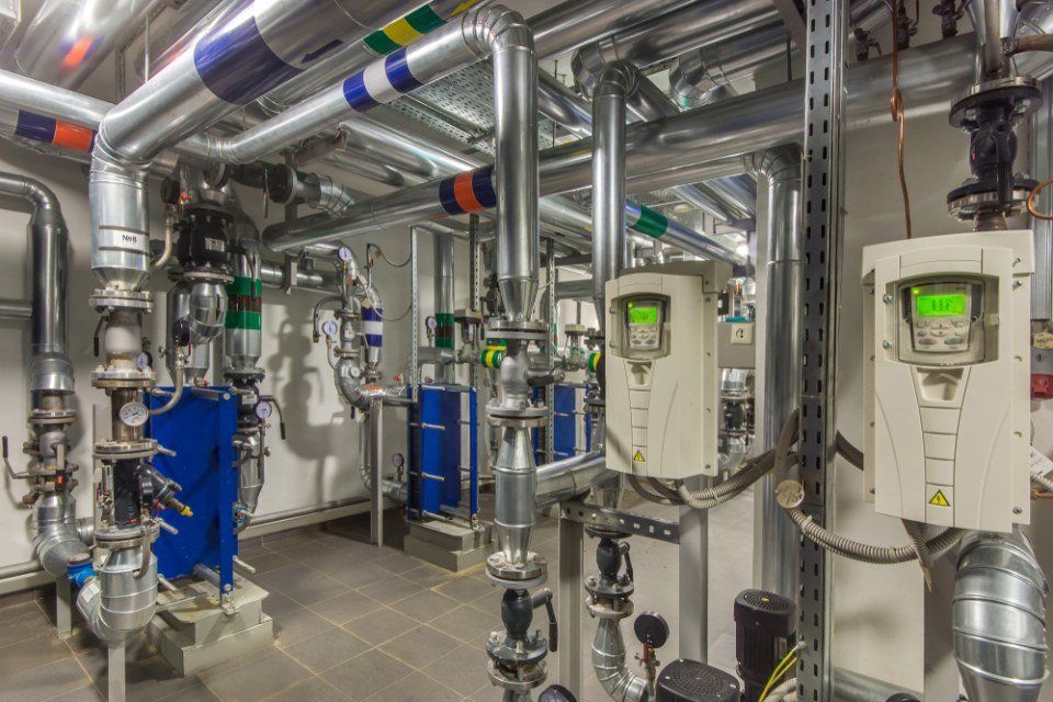 Locale tecnico industriale con tubazioni, valvole e pannelli di controllo bianchi in acciaio inox con display verdi.