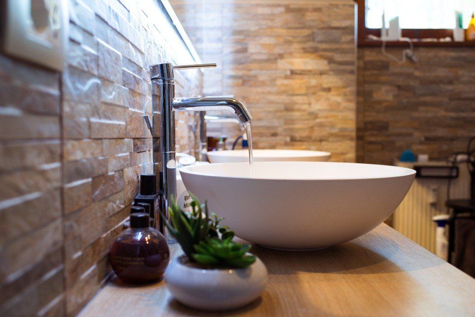 Lavabo moderno con rubinetto cromato, vasca bianca e piccola pianta in vaso su un piano in legno.