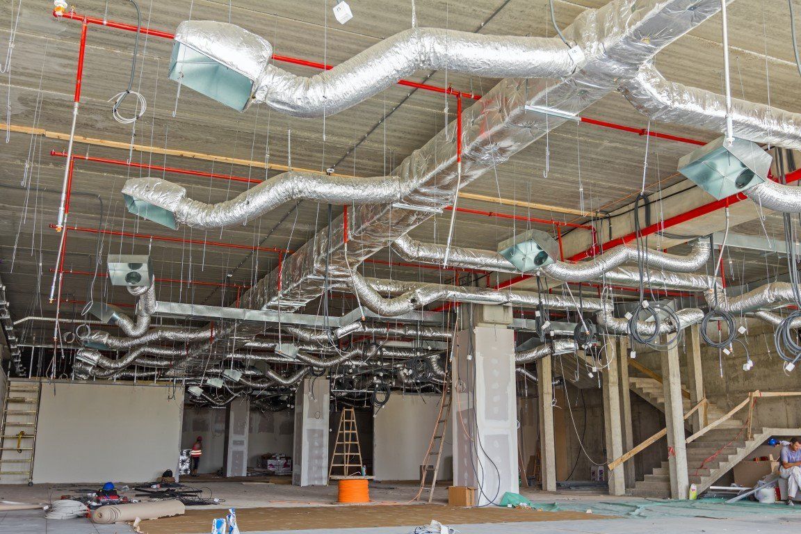 Cantiere edile interno con condotti, tubature e struttura del soffitto a vista e non rifinita.