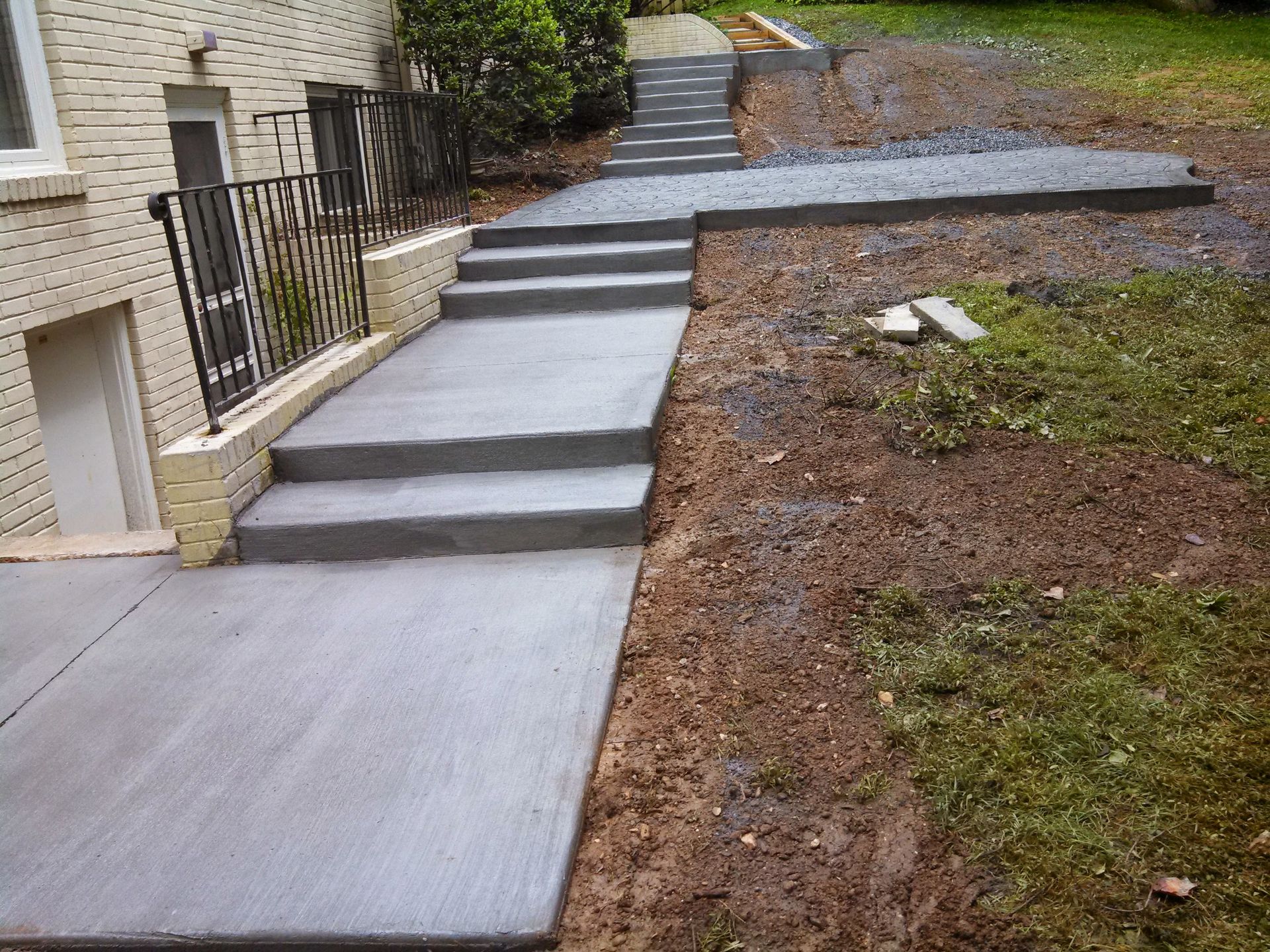 Concrete ramp and steps beside a home, bordered by a black railing and brown mulch landscaping.