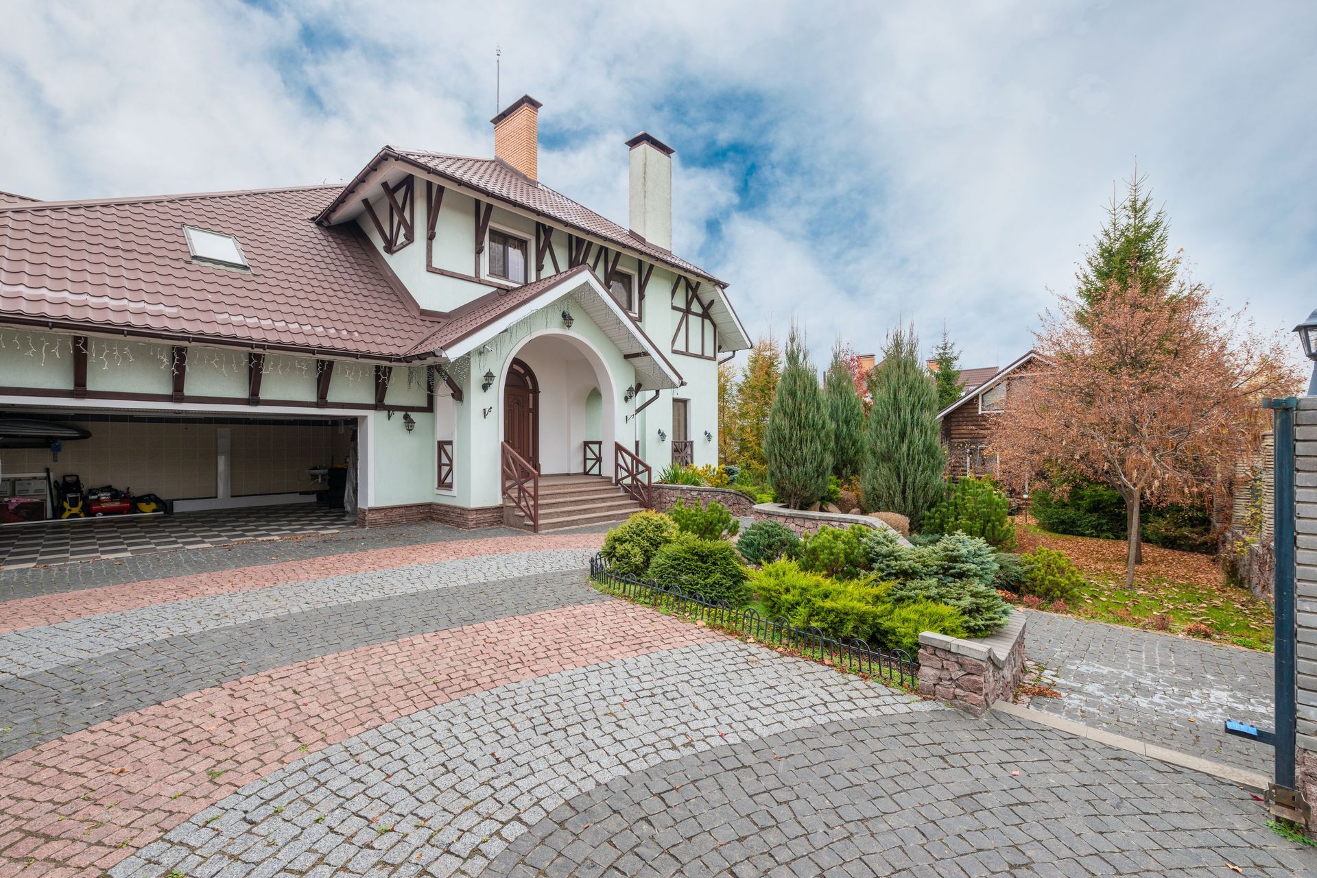 Large white house with red-tiled roof, arched entrance, and landscaped driveway under a cloudy sky