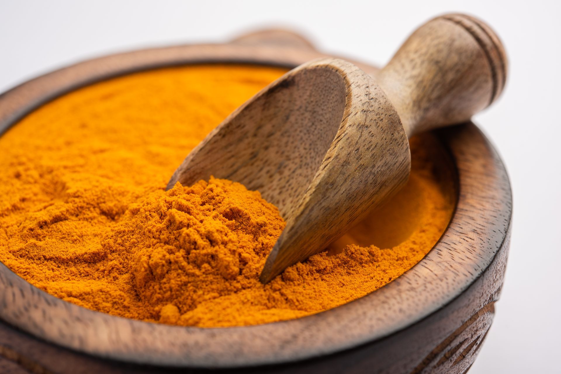 Un mortier et un pilon en bois remplis de poudre de curcuma et une cuillère en bois.