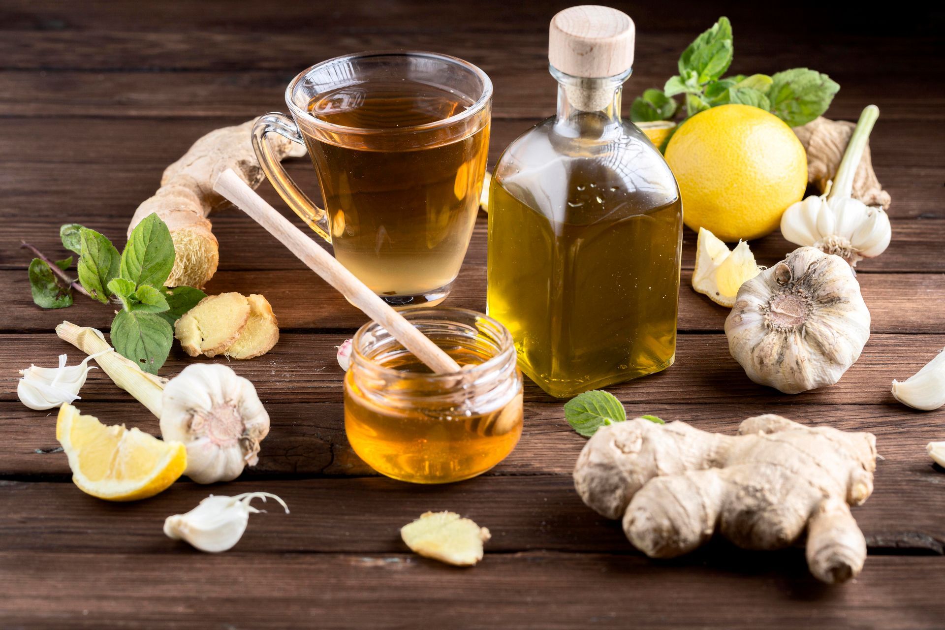 Une table en bois sur laquelle est posée une tasse de thé, de miel, d'ail, de citron et de menthe.
