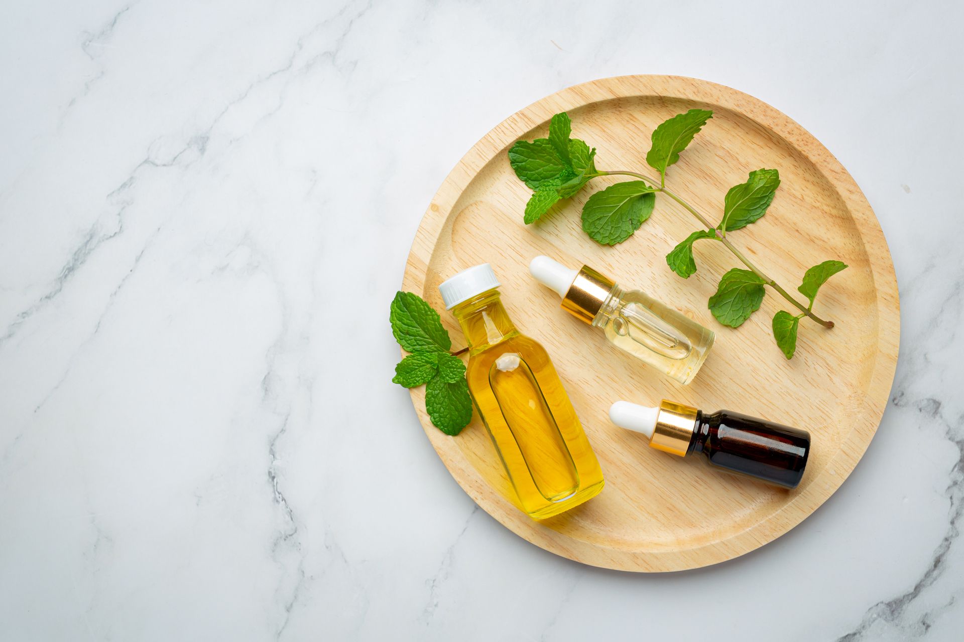 Trois bouteilles d'huiles essentielles et de feuilles de menthe sur un plateau en bois.