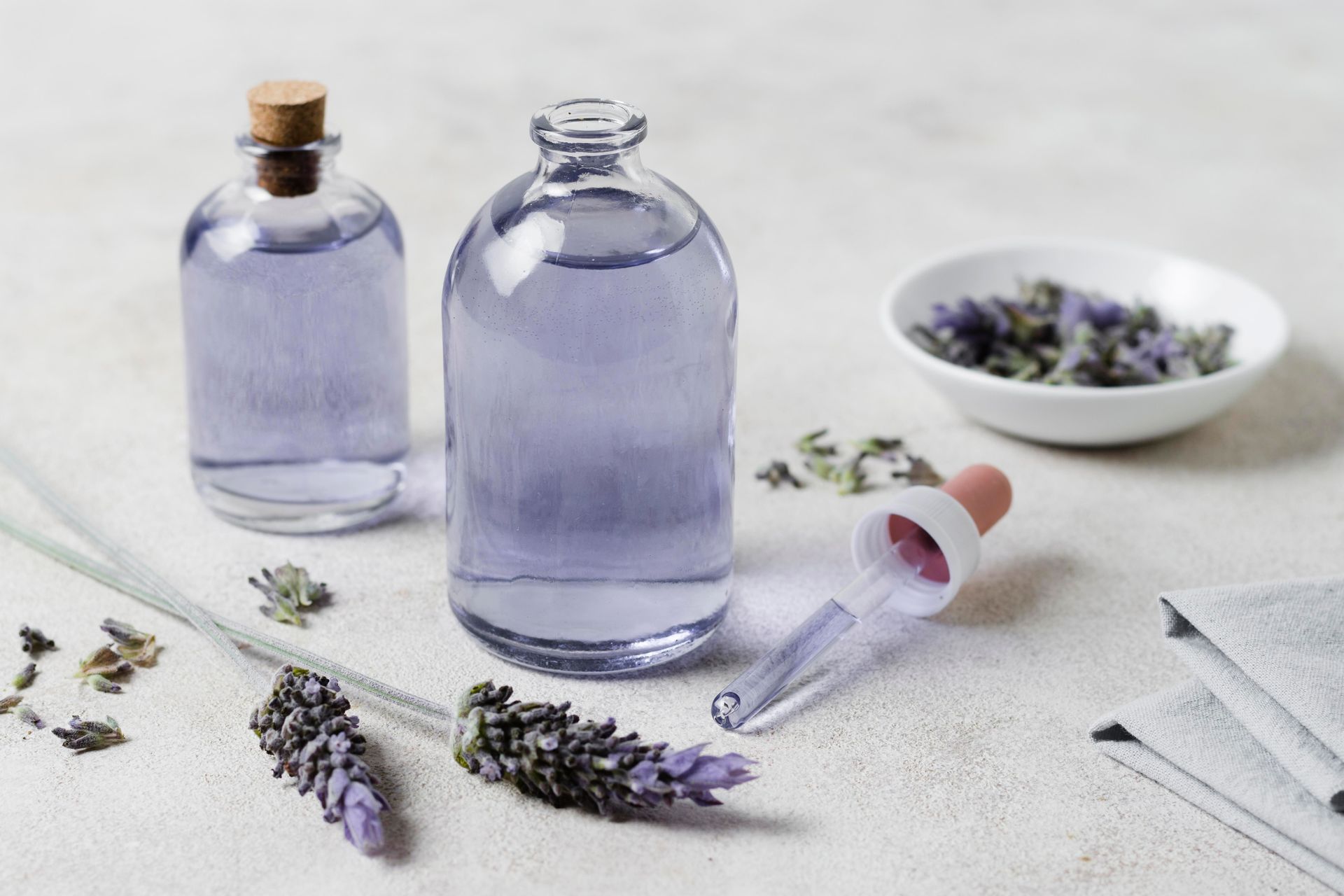 Un flacon d'huile essentielle de lavande à côté d'un bol de fleurs de lavande et d'un compte-gouttes.