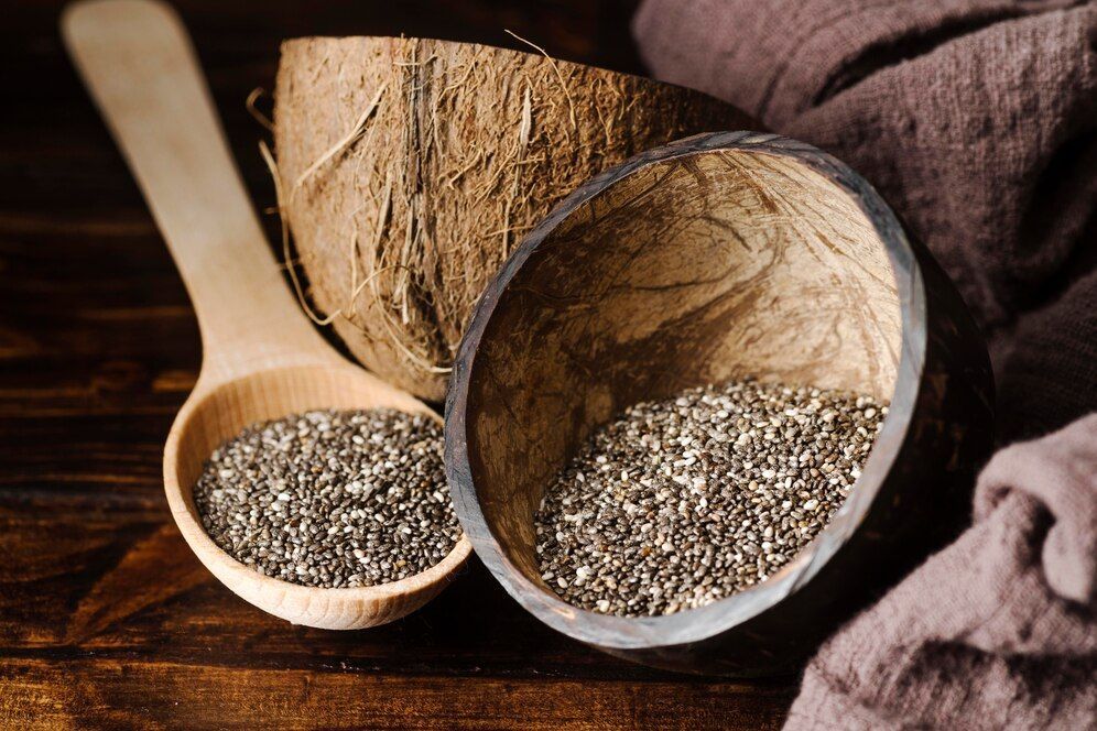 Une cuillère en bois remplie de graines de chia à côté d'une noix de coco sur une table en bois.