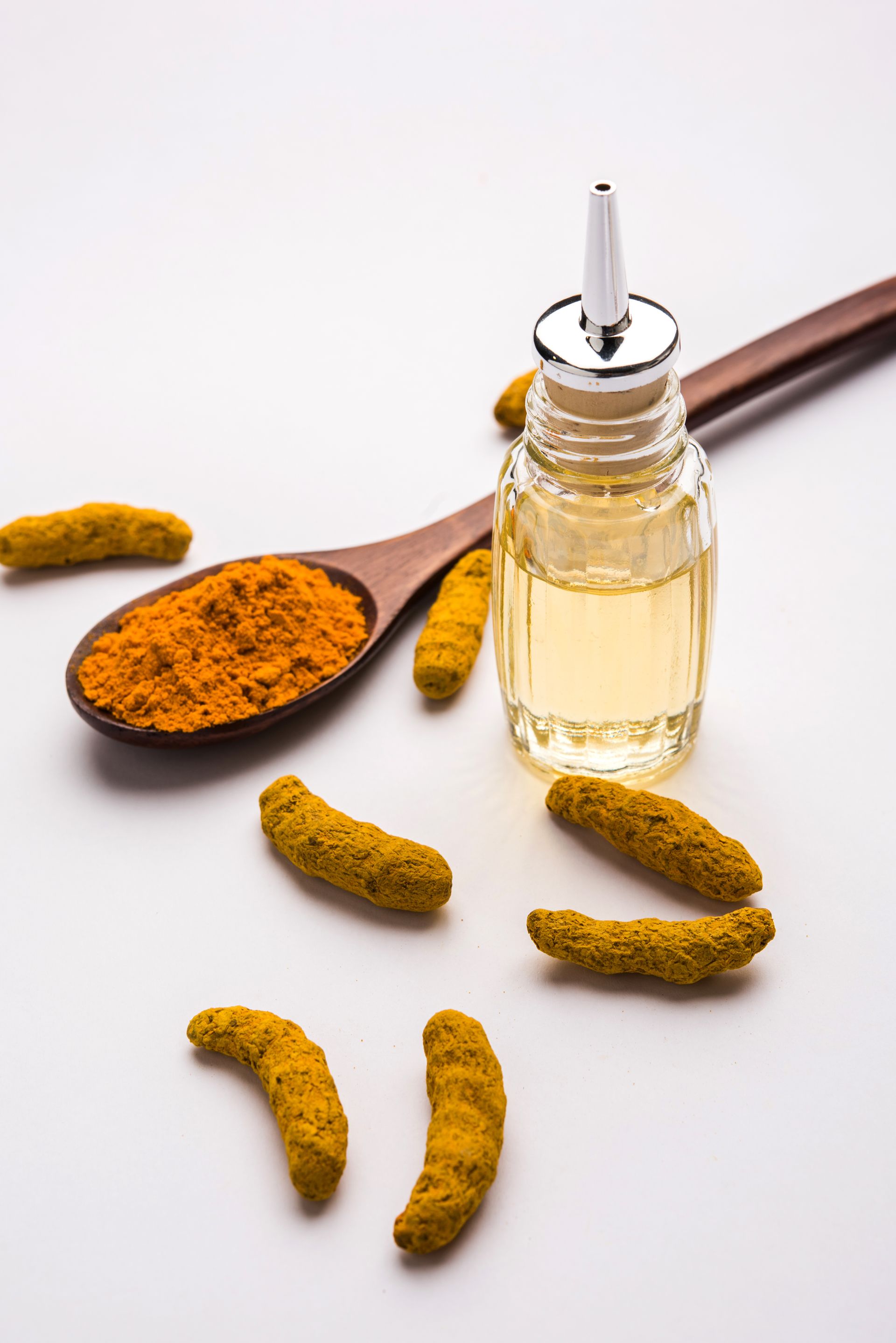 Une cuillère en bois remplie de poudre de curcuma à côté d'une bouteille d'huile de curcuma.