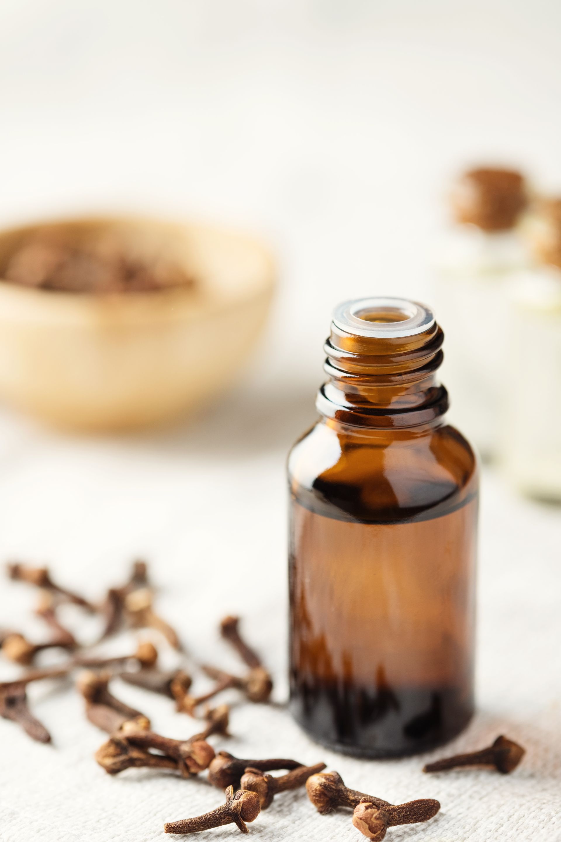 Il y a une bouteille d'huile essentielle à côté d'un bol de clous de girofle.