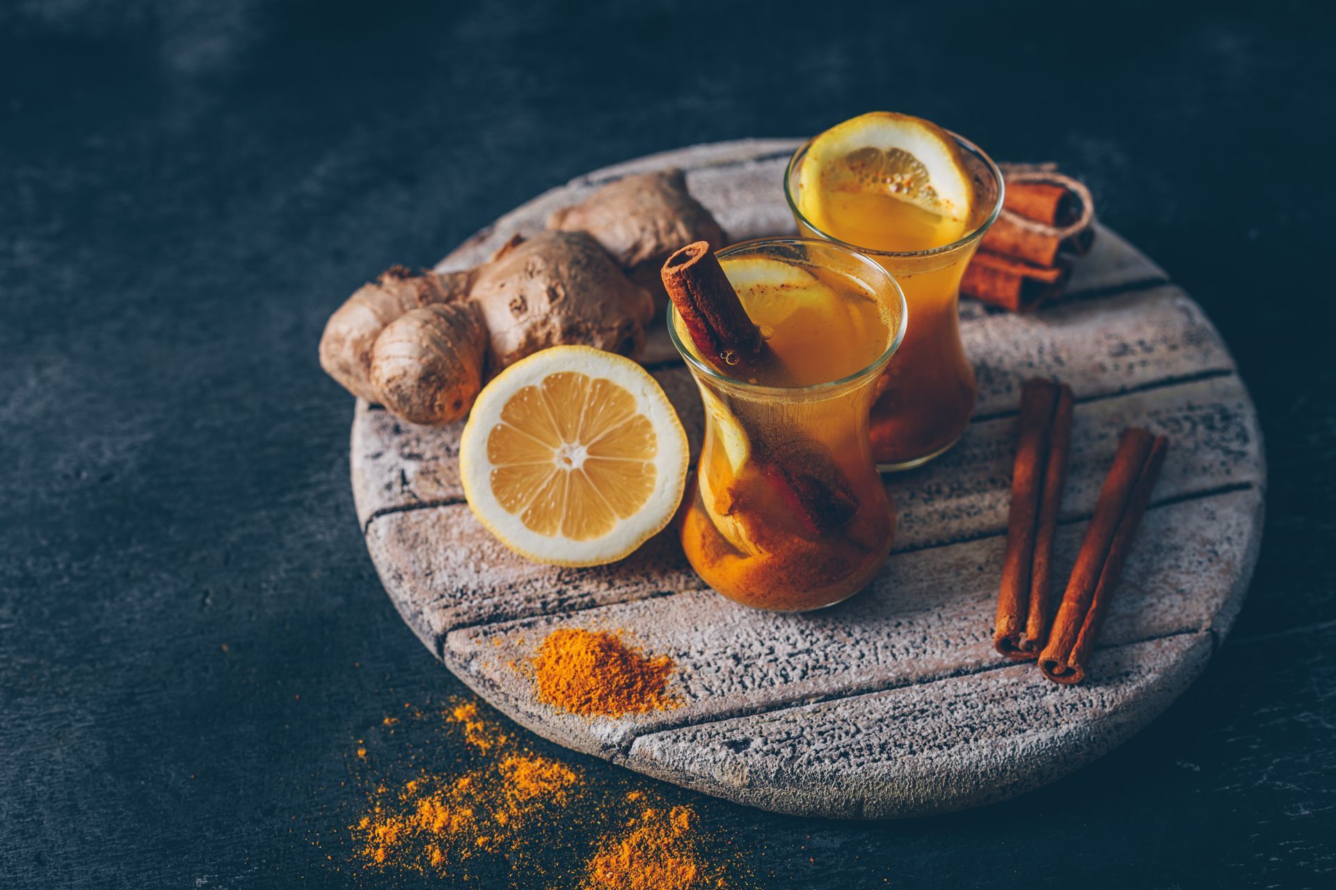Deux verres de soda au gingembre avec du citron, des bâtons de cannelle et du curcuma sur une planche à découper en bois.