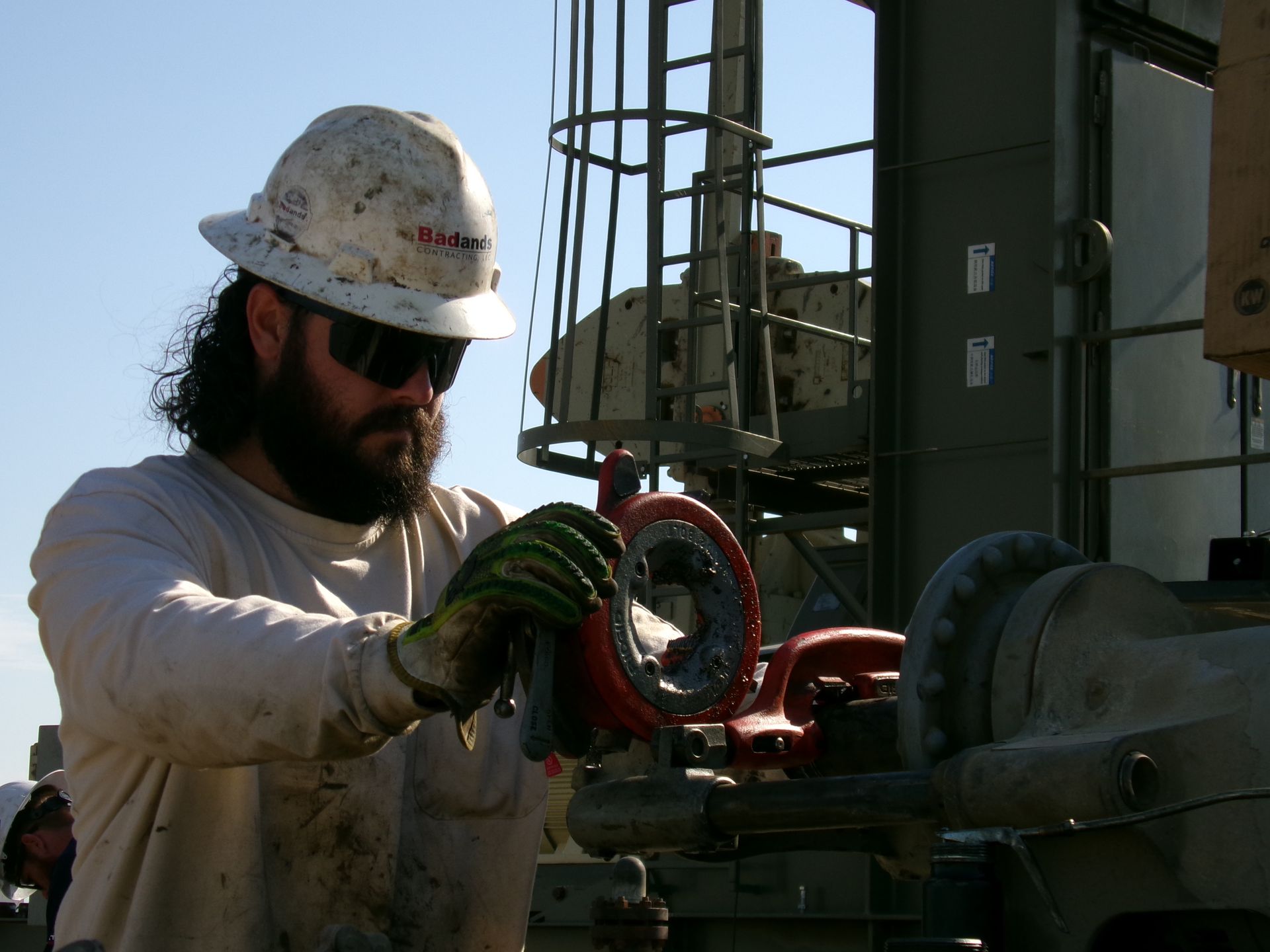 Worker in hard hat and gloves handling red pipe fittings at an industrial site.