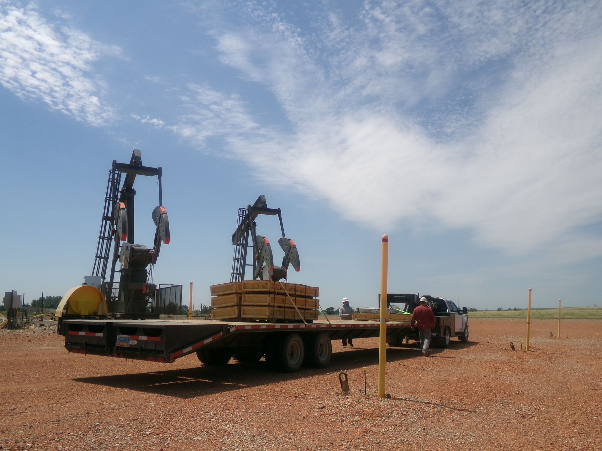 Flatbed truck carrying farm machinery in a gravel lot under a cloudy sky