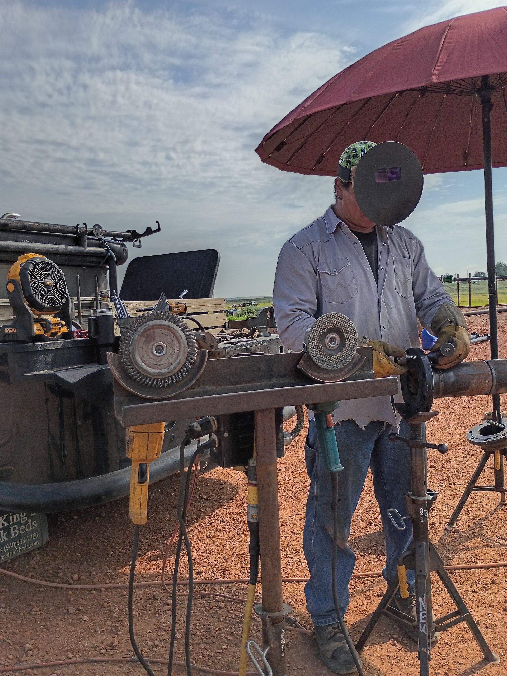 Person in a hat grilling food under a red umbrella beside a truck on a cloudy day