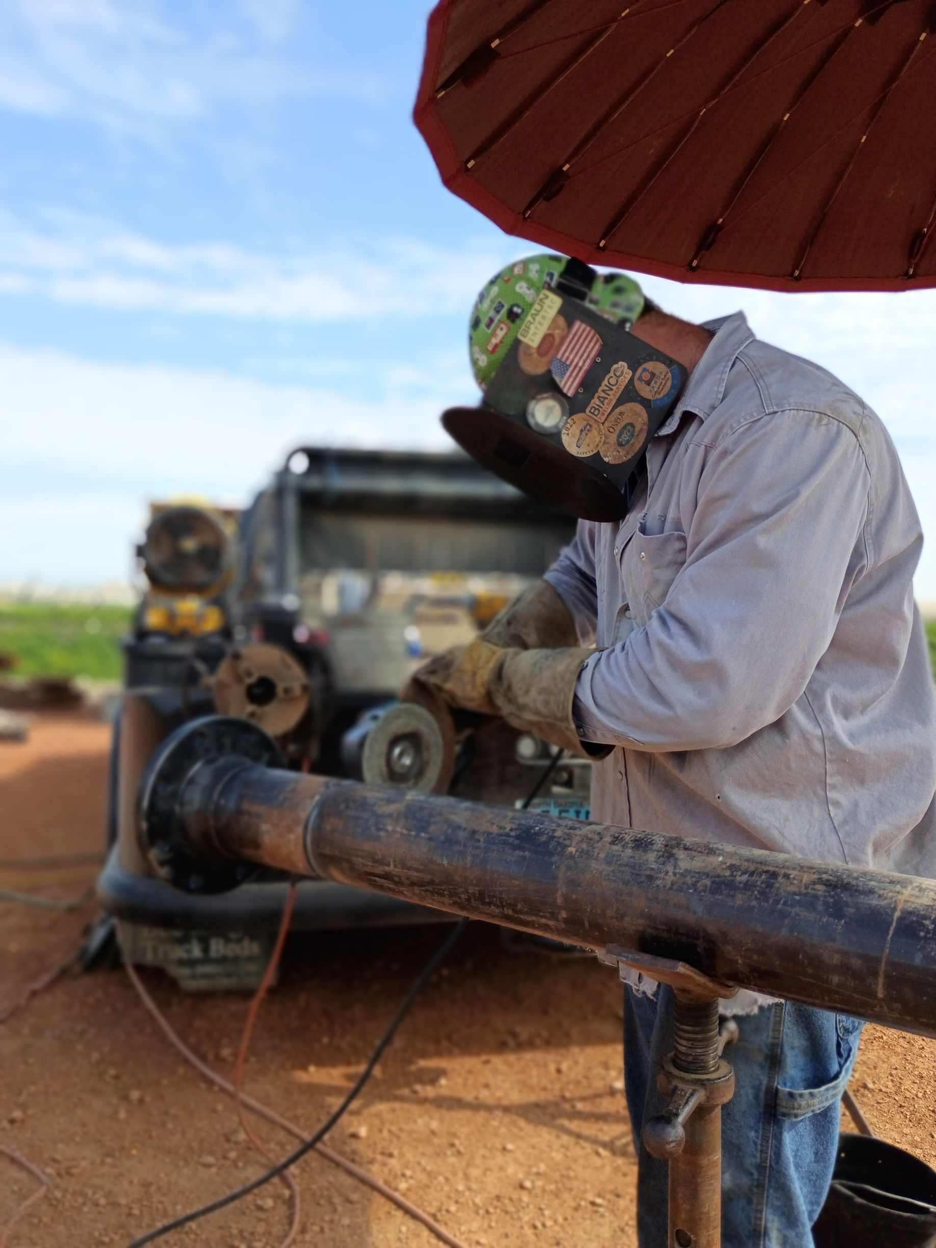 Person working with a pipe near a vehicle under a red umbrella in a dry outdoor field