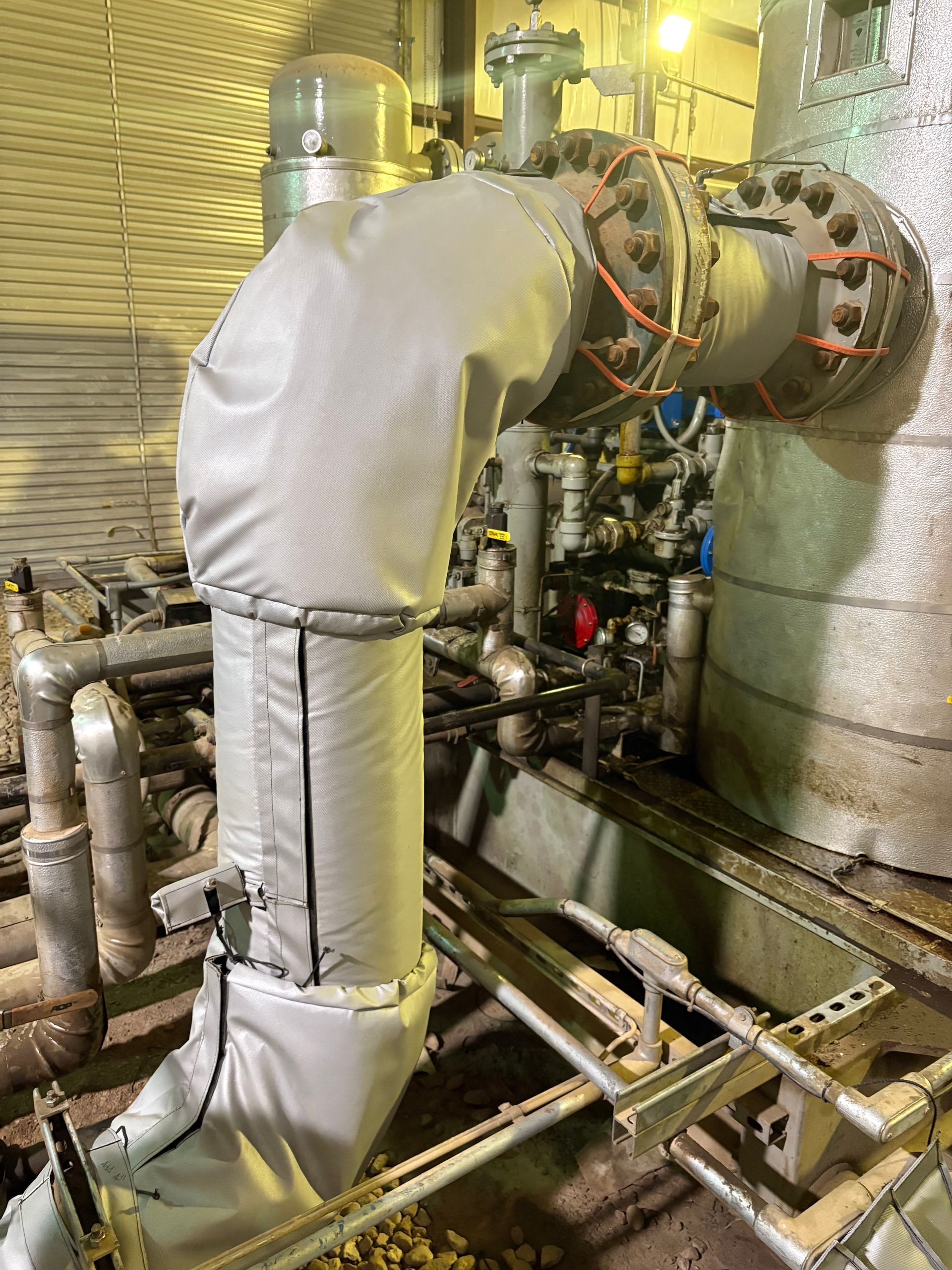 Industrial piping with an insulated duct connected to a large metal vessel in a plant room
