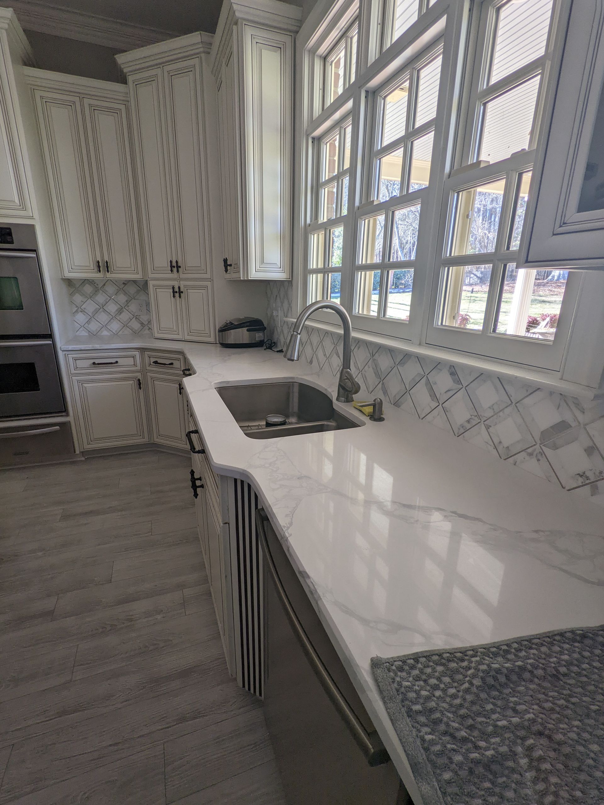 Kitchen with white cabinets, large window, and stainless steel sink.