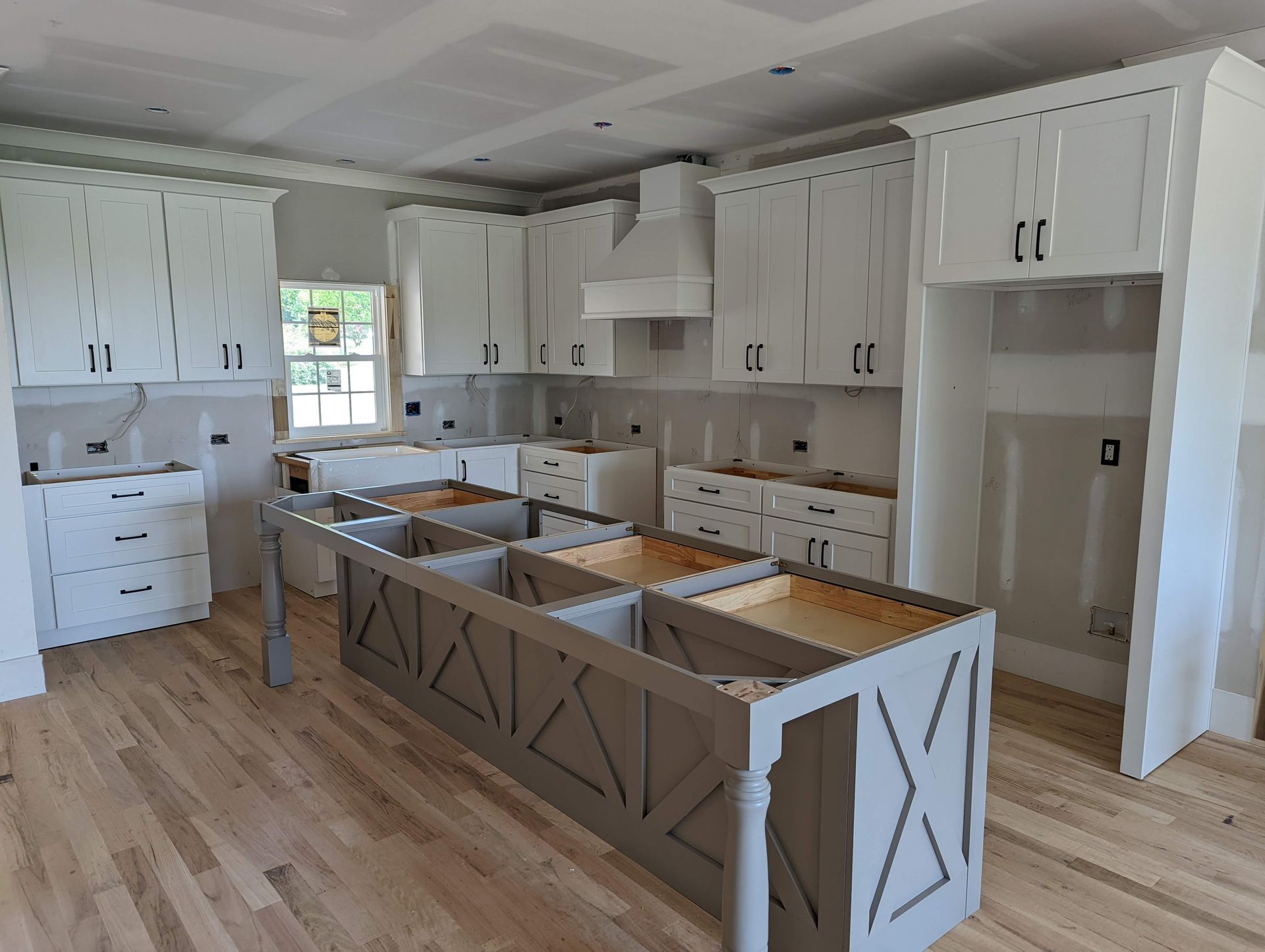 New kitchen with white cabinets, gray island, and wood flooring.