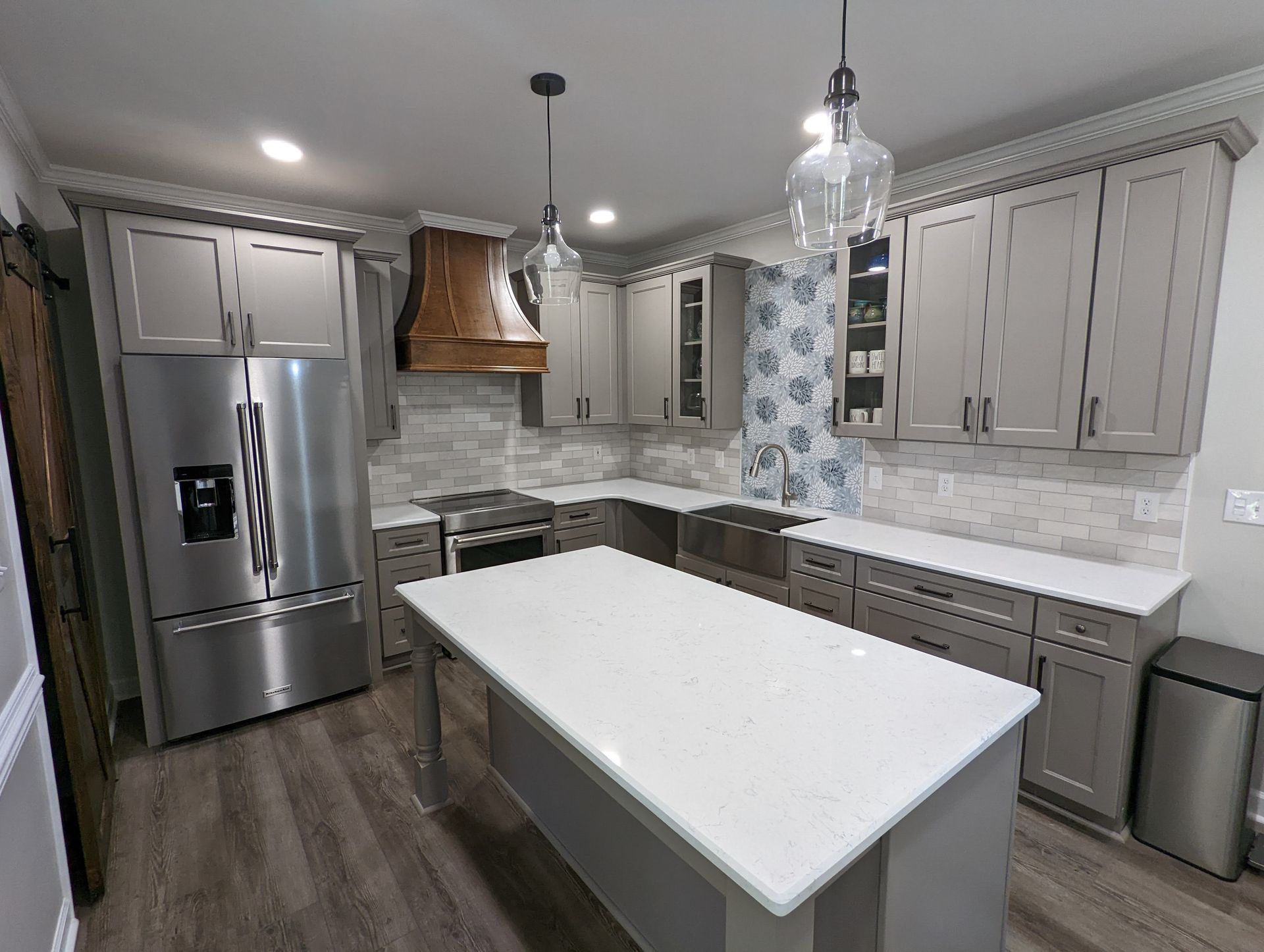 Modern kitchen with gray cabinets, stainless steel appliances, white countertops, and a large island.