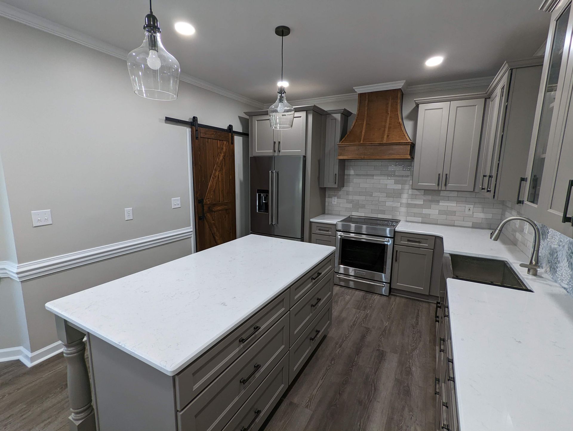 Gray kitchen with white countertops, a wooden range hood, and a kitchen island. A barn door is visible.