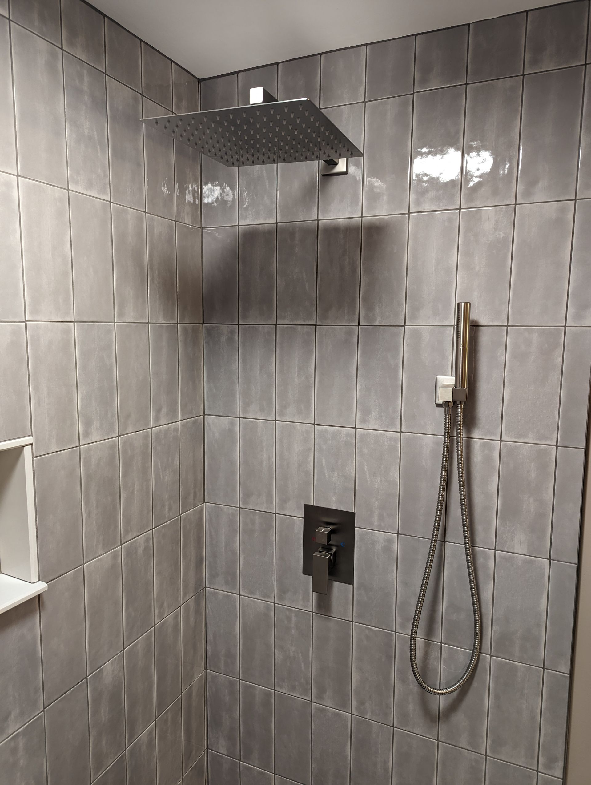 Gray tiled shower with square rain shower head and handheld sprayer.
