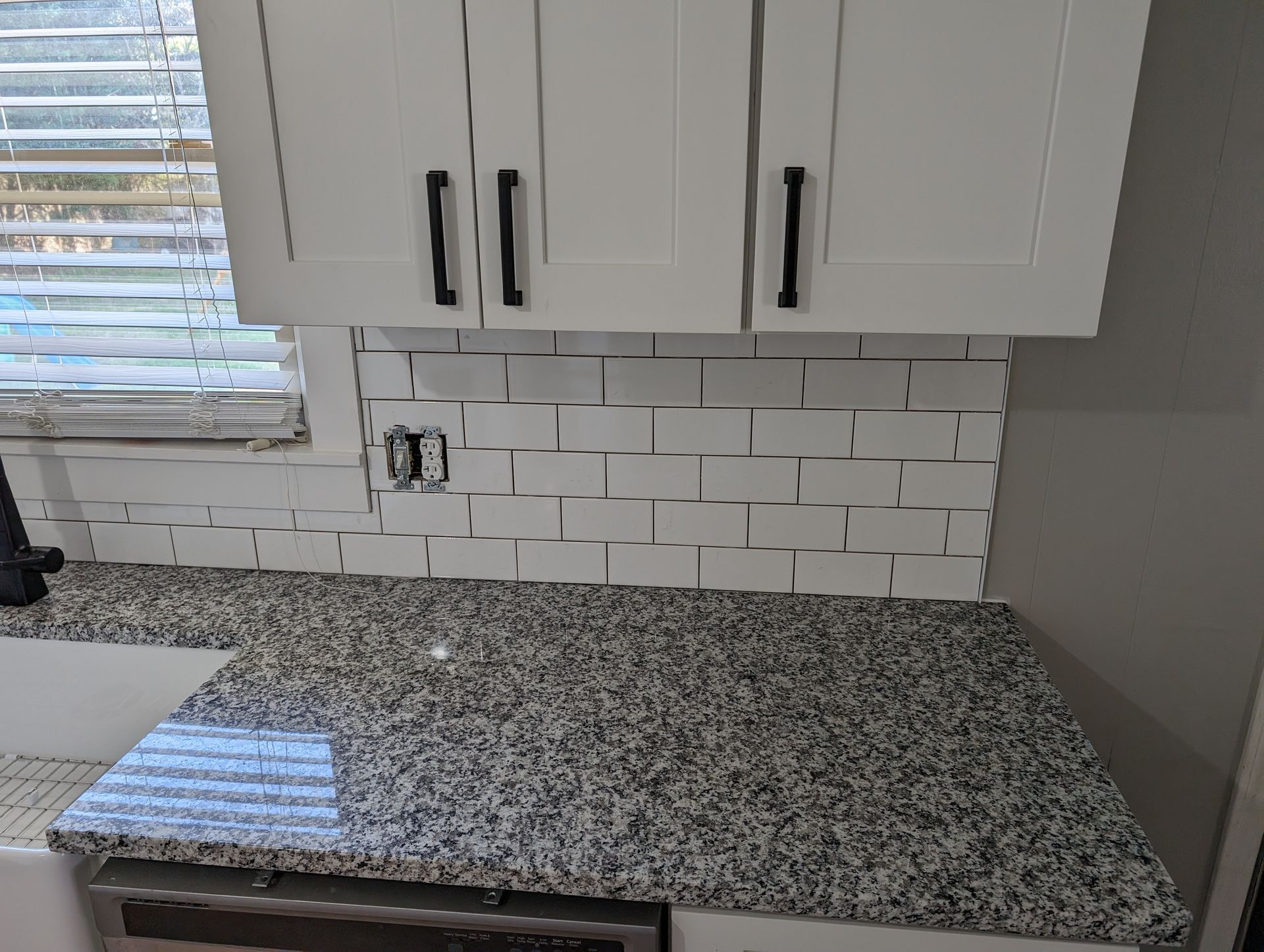 Kitchen with white cabinets, gray granite countertop, white subway tile backsplash, and black hardware.