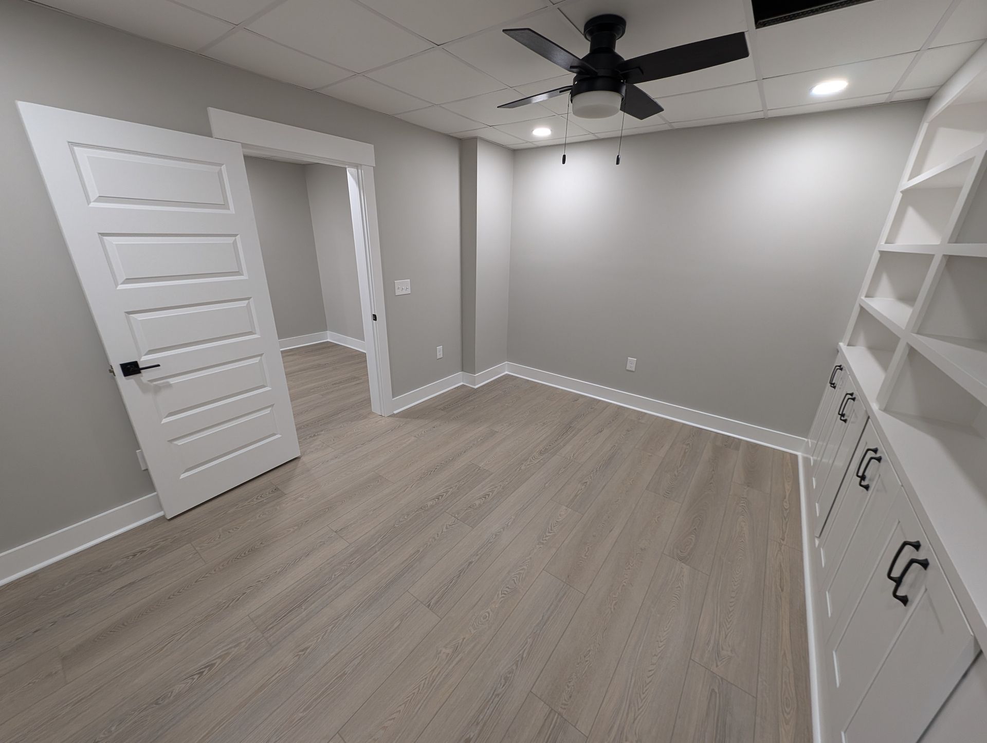 Empty room with grey walls, wood-look flooring, and ceiling fan.
