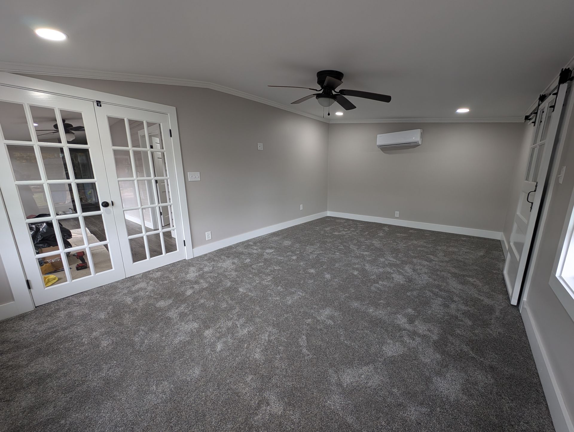 An empty room with gray carpet, white trim, French doors, and a ceiling fan. The walls are painted a light gray.