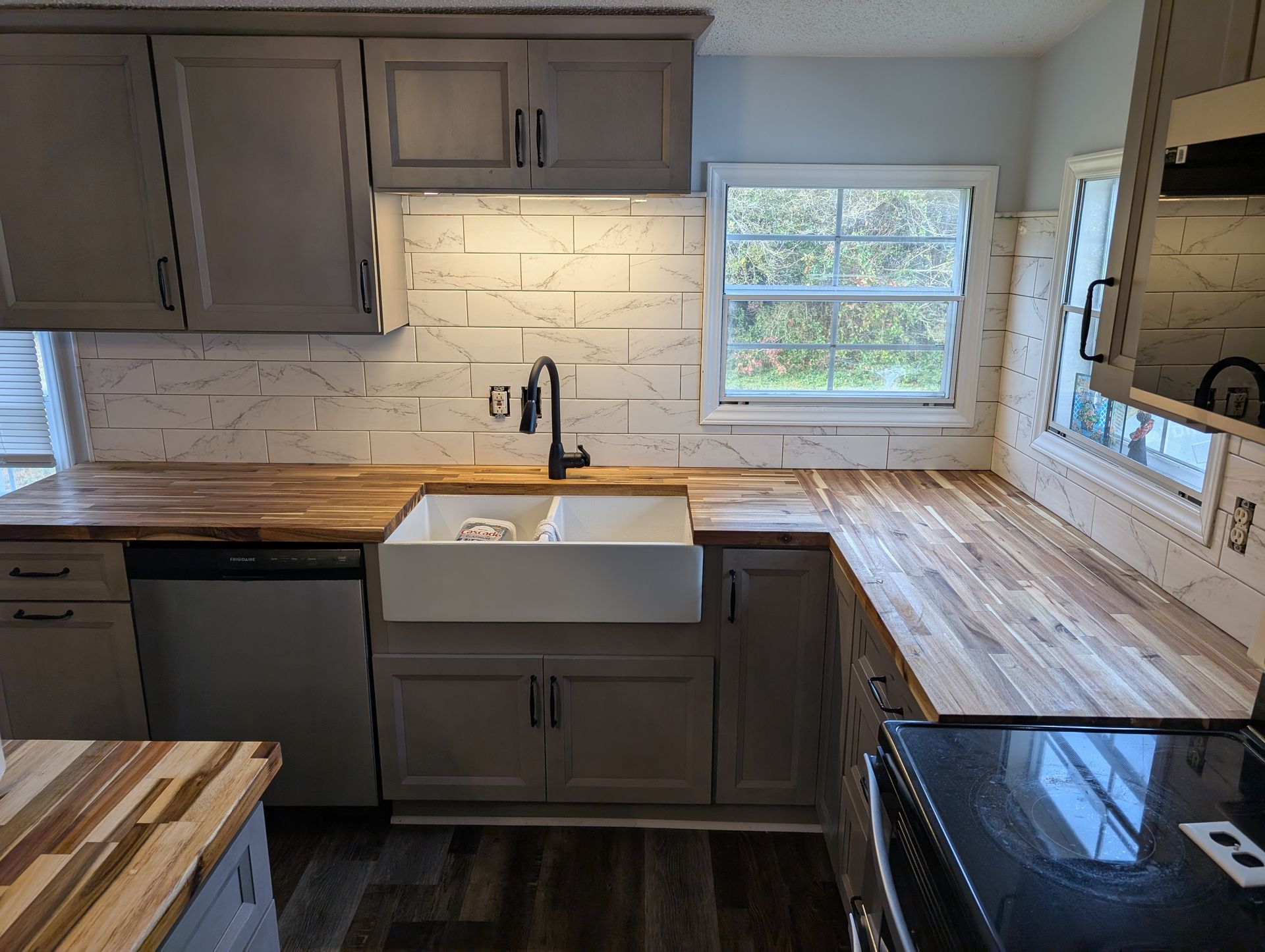 Gray kitchen with butcher block countertops, a white farmhouse sink, and a window above the sink.
