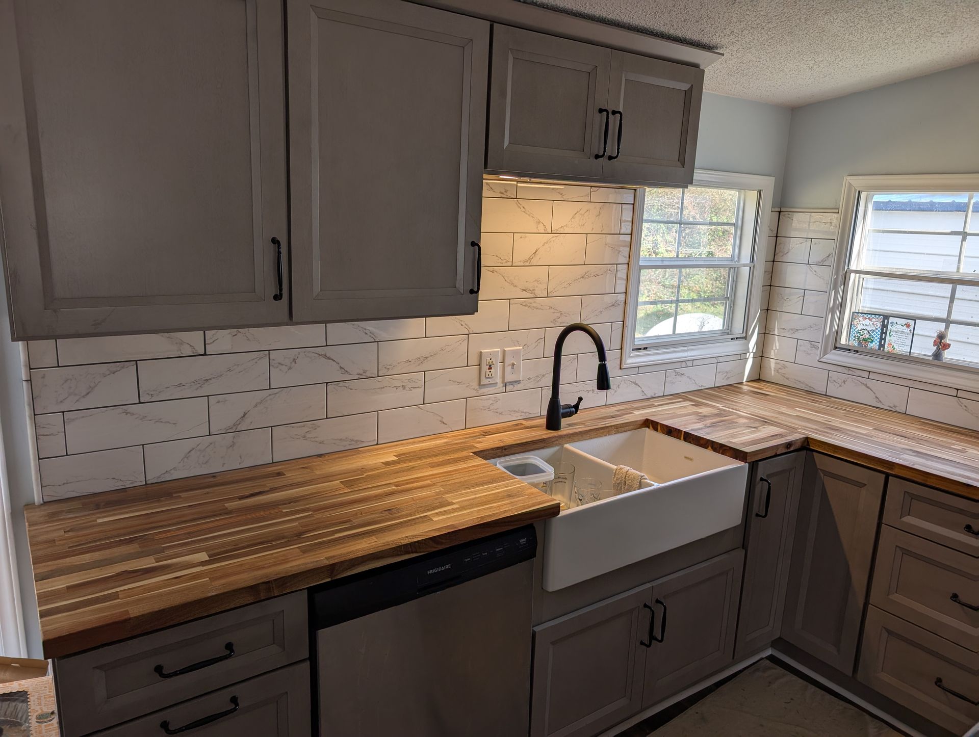 A kitchen with light gray cabinets, butcher block countertops, white subway tile backsplash, and a farmhouse sink.