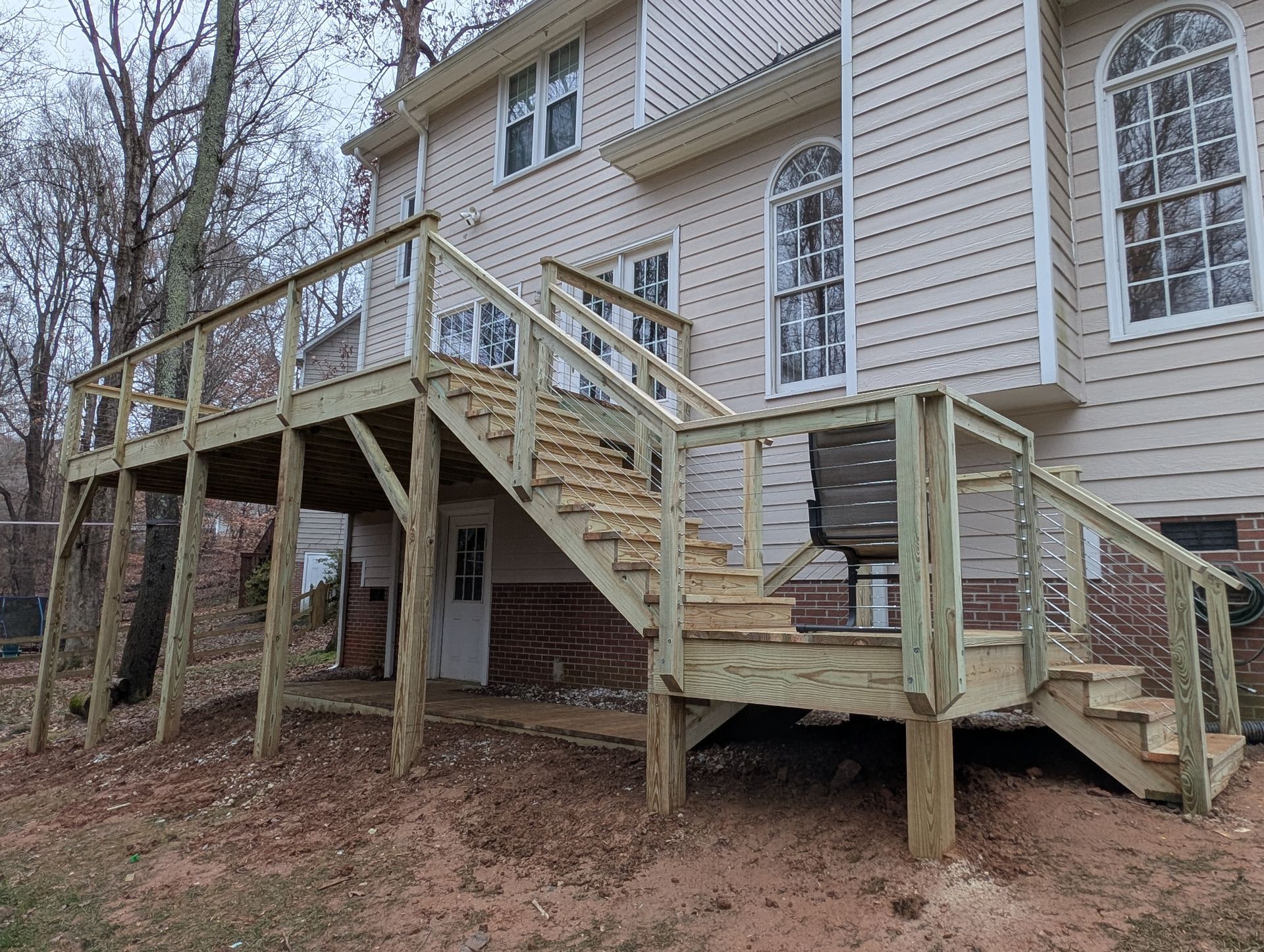 Wooden deck with stairs attached to a two-story house. The deck is elevated and appears to be newly built.