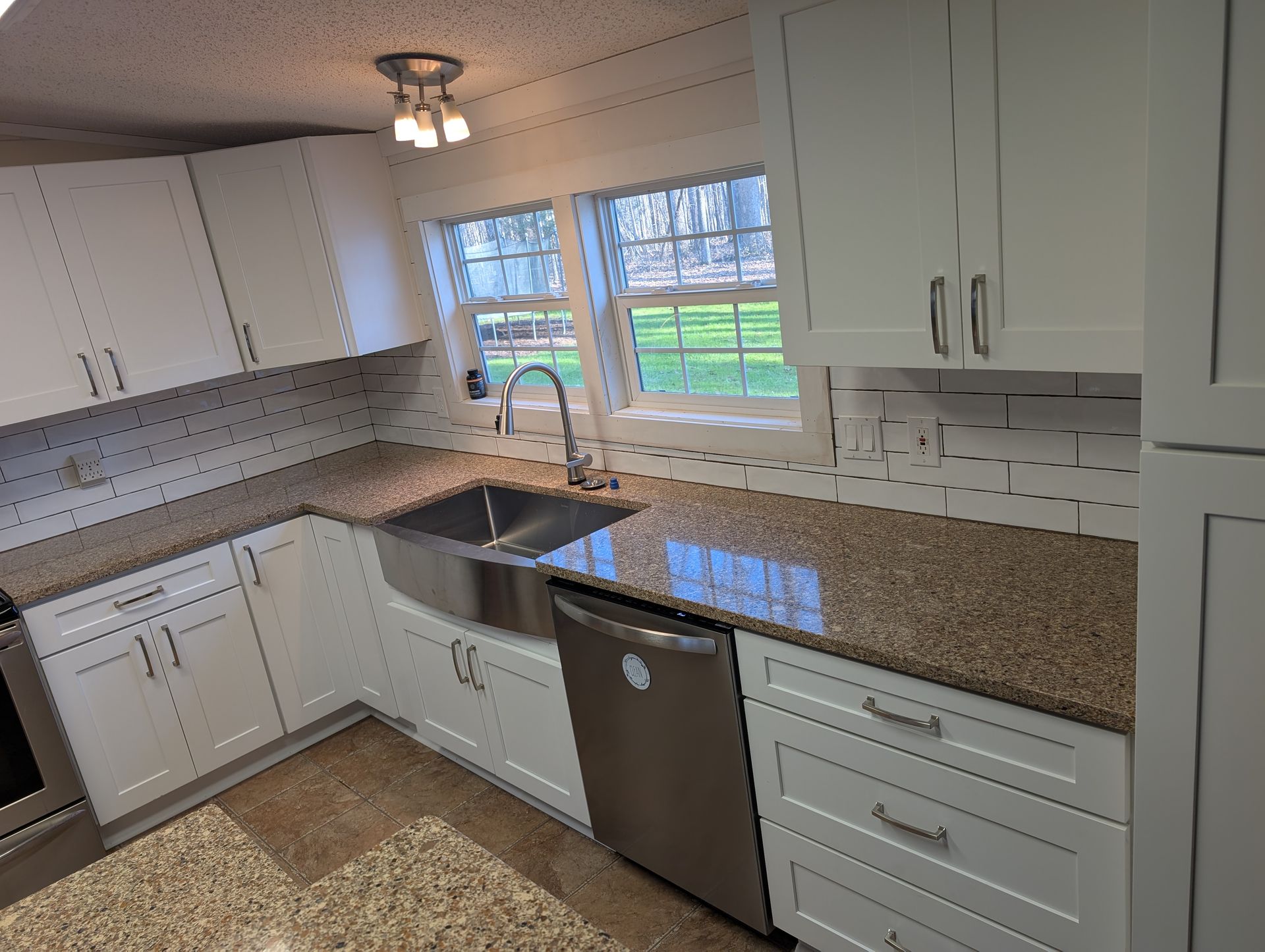 White kitchen with granite countertops, stainless steel sink and appliances, and a window with a view.