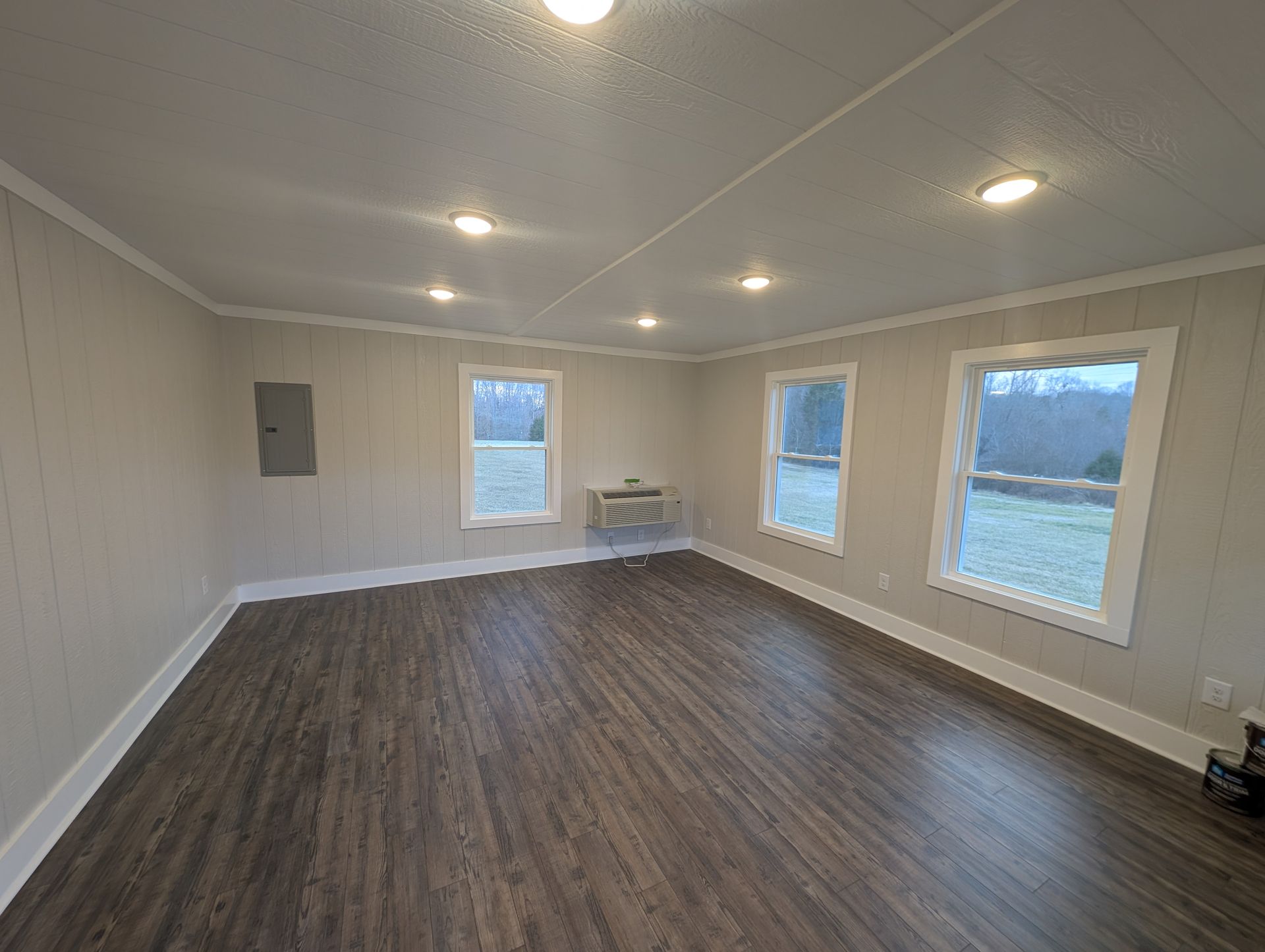 Empty interior room with dark wood-look floors, gray walls, white trim, multiple windows, and recessed lighting.