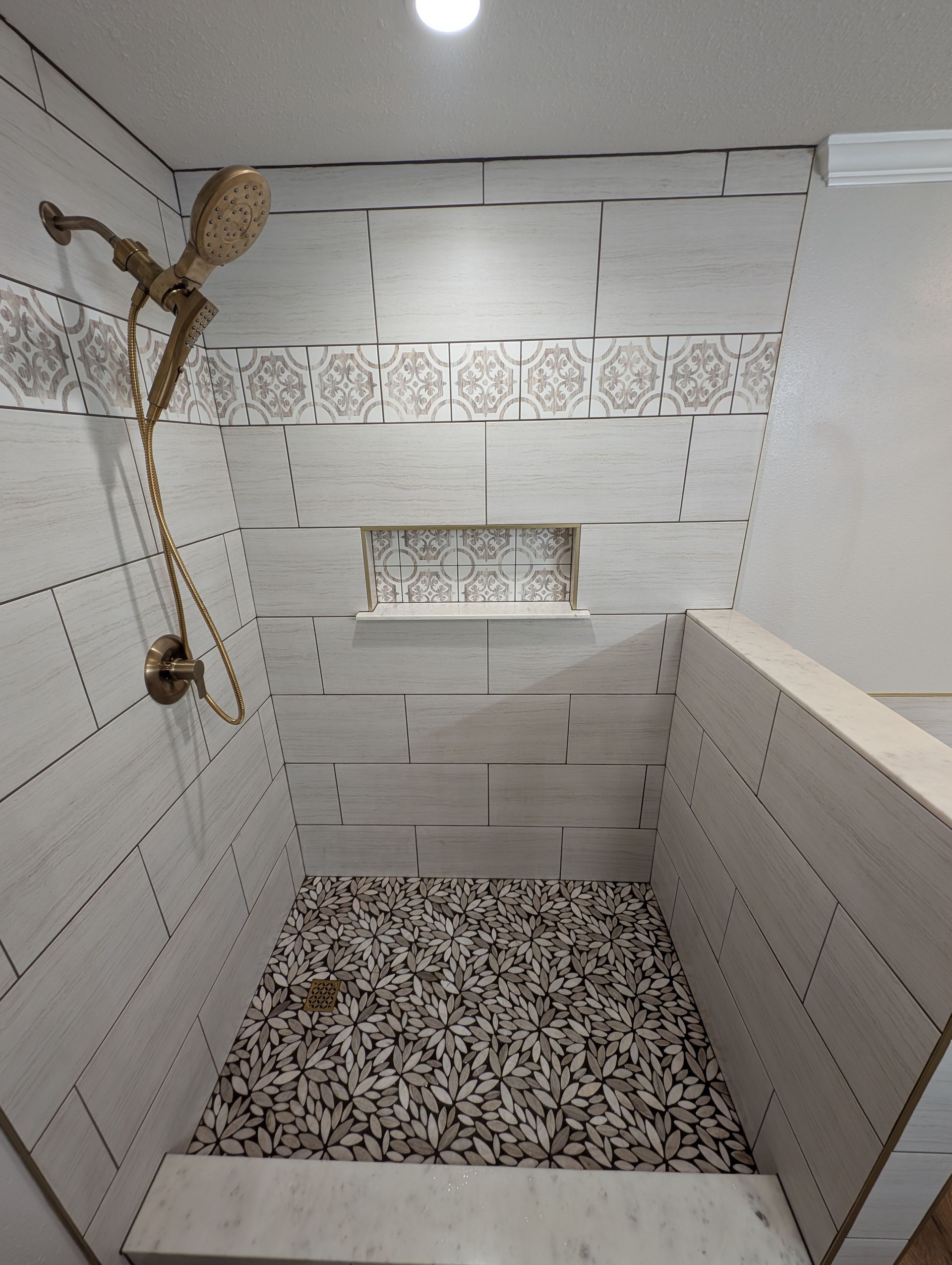 A newly tiled shower with a decorative mosaic floor, patterned accent tiles, and a gold showerhead.