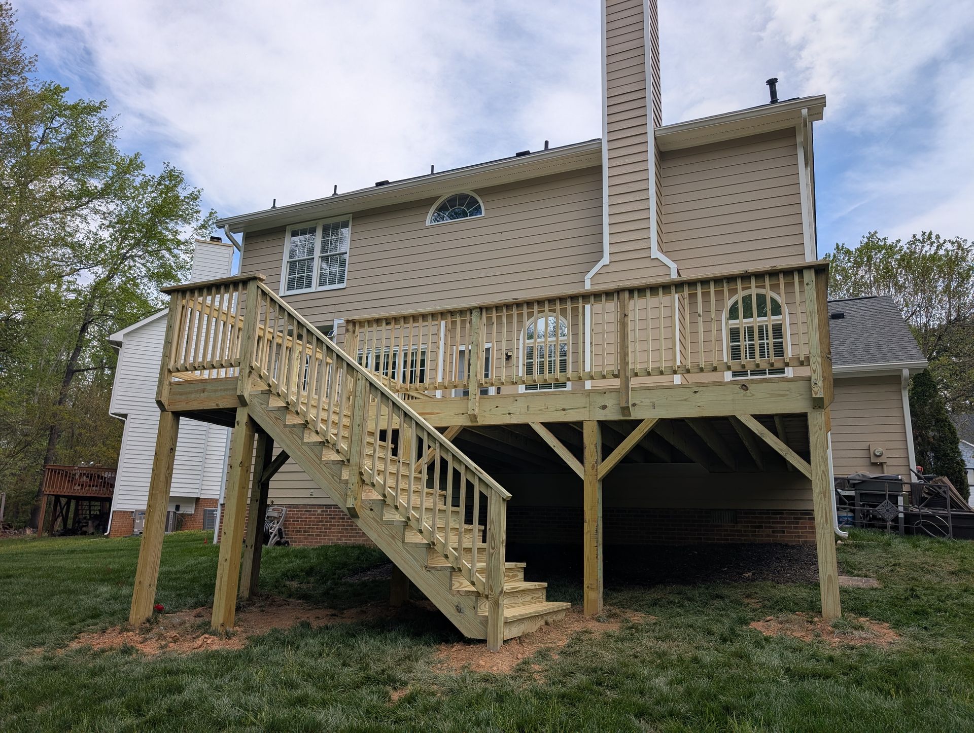 Wooden deck with stairs attached to the back of a two-story house, set on a grassy lawn.