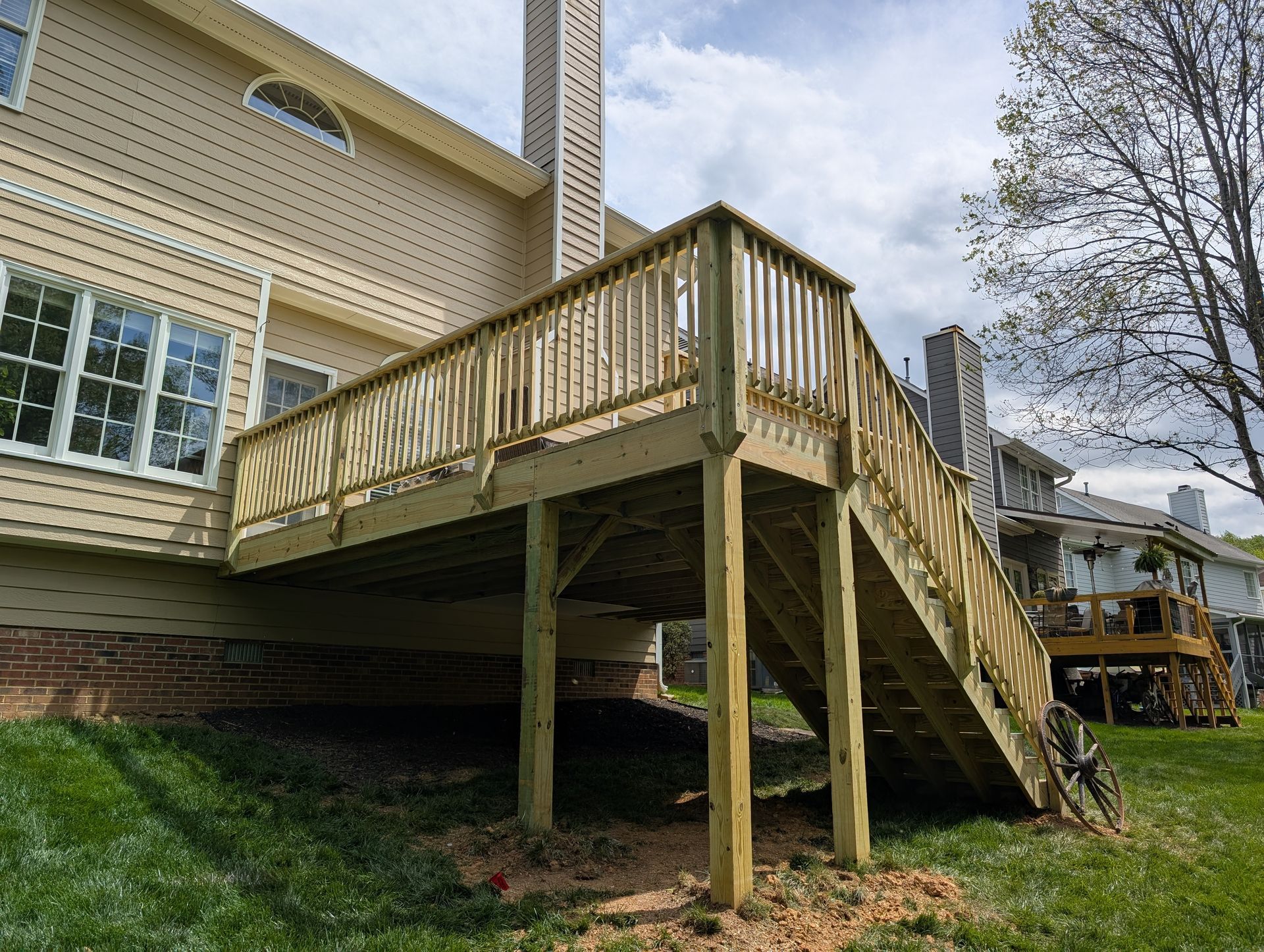 Wooden deck attached to a two-story beige house with a staircase leading down to the yard.