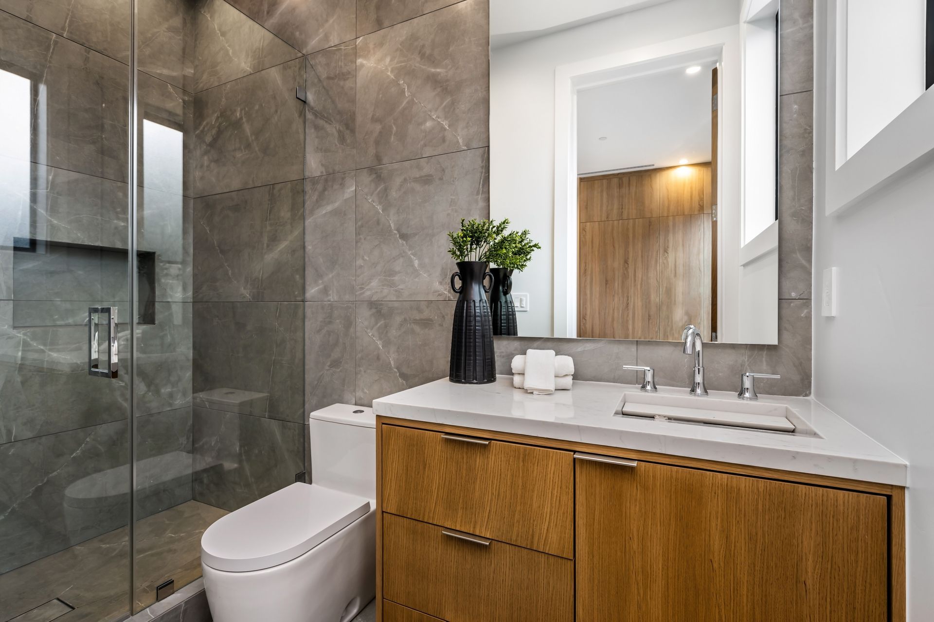 Modern bathroom featuring a glass shower, toilet, wooden vanity with a white countertop, and a mirror.