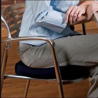 Persona seduta su una sedia di metallo, con indosso una camicia azzurra e pantaloni grigi, con le mani giunte.