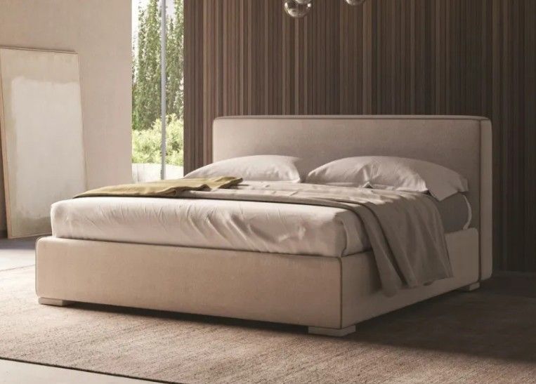 Moderno letto imbottito beige in una camera da letto minimalista con luce naturale soffusa.