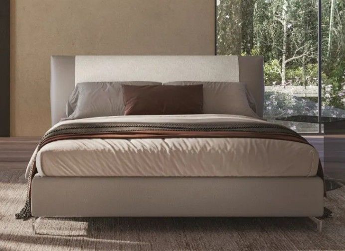 Letto imbottito moderno con biancheria da letto grigia e marrone in una camera da letto minimalista accanto a una grande finestra