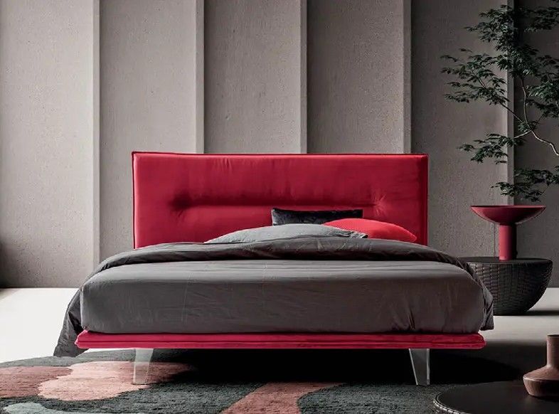 Camera da letto moderna con letto imbottito rosso e biancheria da letto grigia su una parete neutra.
