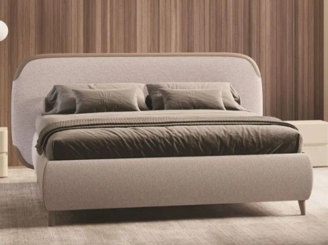 Letto imbottito moderno color beige con lenzuola grigie, appoggiato a una parete rivestita in legno in una camera da letto minimalista.