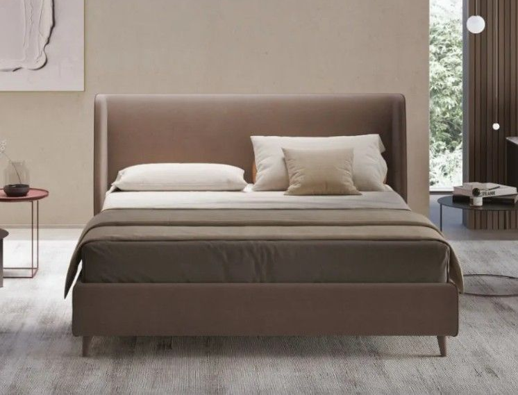 Camera da letto minimalista con letto imbottito color tortora, cuscini bianchi e arredamento neutro.