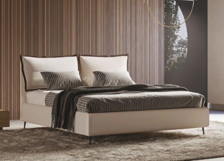 Moderno letto imbottito beige con lenzuola e cuscini a righe in una camera da letto minimalista