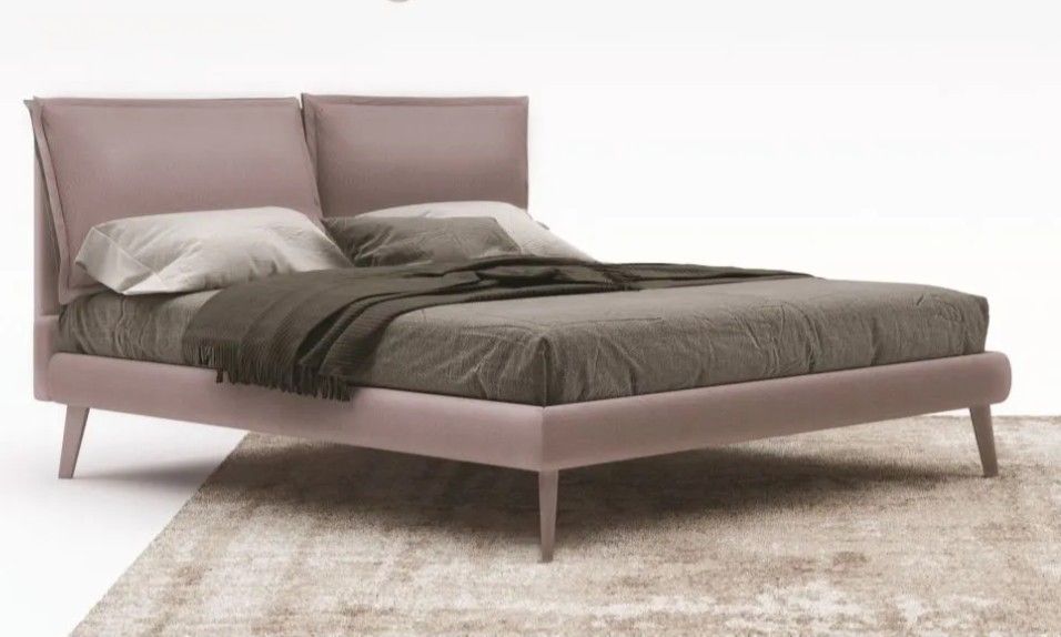 Letto imbottito moderno con testiera, biancheria da letto grigia e struttura rosa chiaro su sfondo bianco.