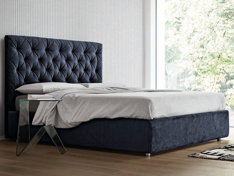 Camera da letto moderna con testiera imbottita scura, biancheria da letto grigia e luminosa luce naturale proveniente da una finestra.