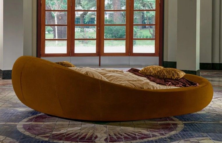 Divano lounge curvo color giallo senape in una stanza moderna con ampie finestre e tappeto a motivi geometrici.