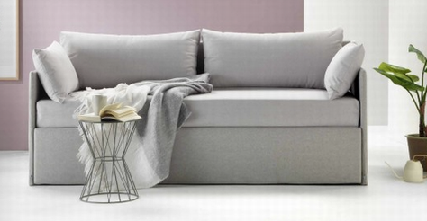 Moderno divano grigio con coperta drappeggiata, cuscino, tavolino e pianta in vaso in una stanza minimalista