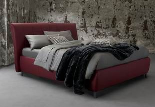 Letto imbottito rosso con lenzuola grigie e coperta nera in una stanza rustica in cemento.