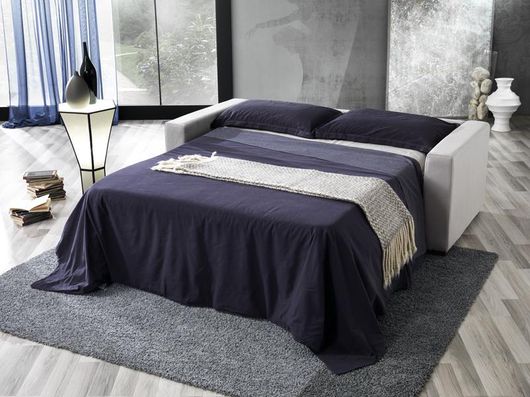Camera da letto moderna con copriletto blu scuro, tappeto grigio e grande finestra con lampada in bianco e nero.